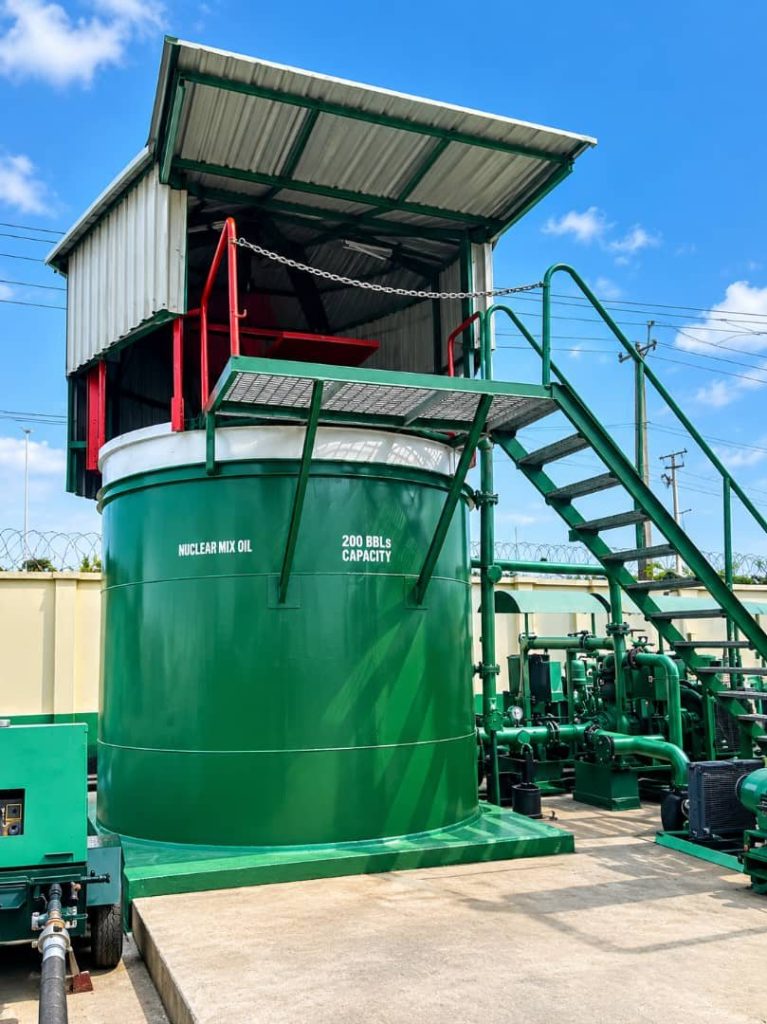 Covered green 200-barrel mixing tank with a stair platform and pumps